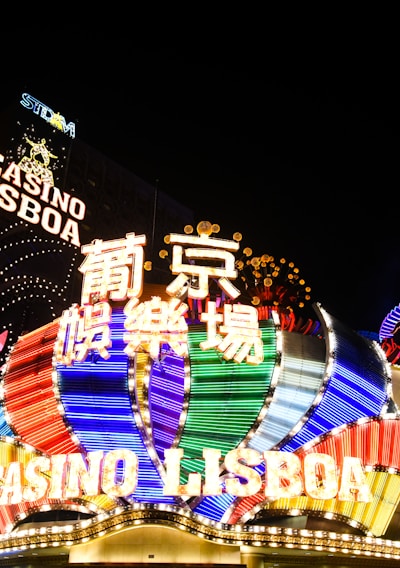Bright neon signs in multiple colors illuminate the night, prominently displaying the name 'Casino Lisboa' alongside signage in Chinese characters. The lights form intricate patterns and vibrant displays, creating a lively and energetic atmosphere.